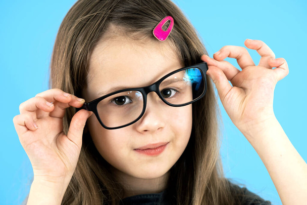 Retrato de cerca de una divertida niña de la escuela con gafas aisladas sobre fondo azul. - Foto, imagen