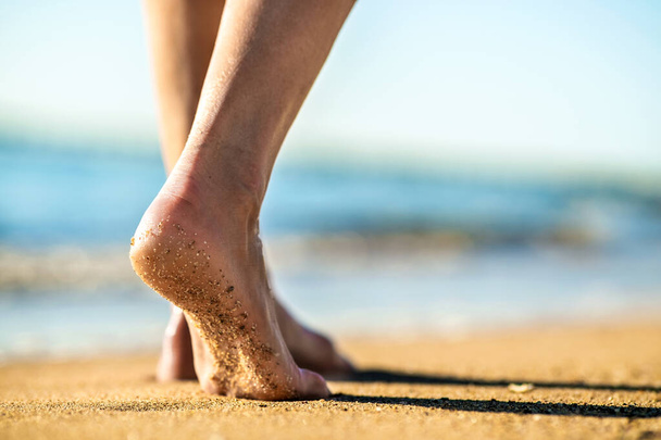 Gros plan des pieds de femme marchant pieds nus sur le sable laissant des empreintes de pas sur la plage dorée. Concept vacances, voyage et liberté. Les gens se relaxent en été. - Photo, image