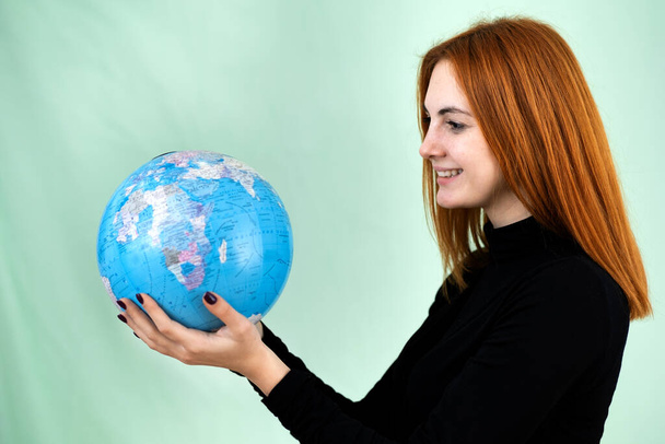 Portrait of a happy young woman holding geographic globe of the world in her hands. Travel destination and planet protection concept. - Foto, afbeelding