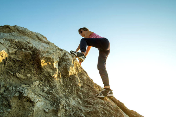 Woman hiker climbing steep big rock on a sunny day. Young female climber overcomes difficult climbing route. Active recreation in nature concept. - Photo, Image
