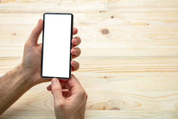 Modélisation d'écran de téléphone portable. Homme tenant un smartphone avec écran blanc vierge, fond en bois, espace de copie
 - Photo, image