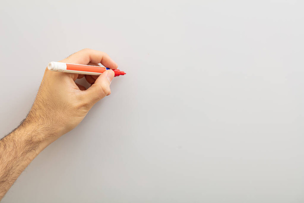 Mano izquierda con un marcador aislado sobre fondo gris. Hombre zurdo sosteniendo un marcador rojo contra pizarra blanca, espacio para copiar
 - Foto, imagen