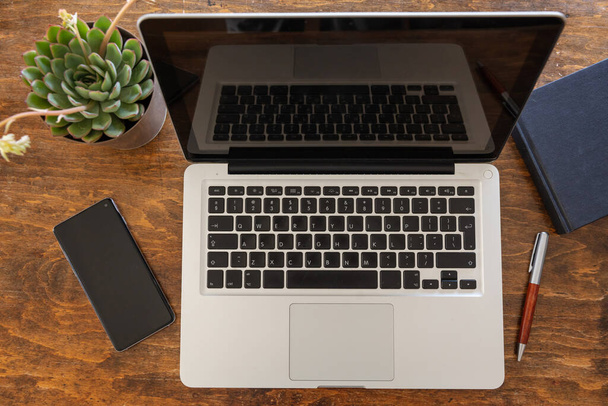 Munkahelyi. Számítógép laptop és mobiltelefon egy fa irodai asztalon, munka otthonról koncepció, felülnézet - Fotó, kép