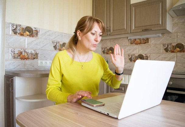 Kobieta dmuchanie pocałunek komunikuje się w czacie online i sieci społecznościowych ze swoimi bliskimi ludźmi siedzącymi w domu w kuchni z laptopów podczas kwarantanny i odległość społeczna w pandemii Coronovirus. - Zdjęcie, obraz