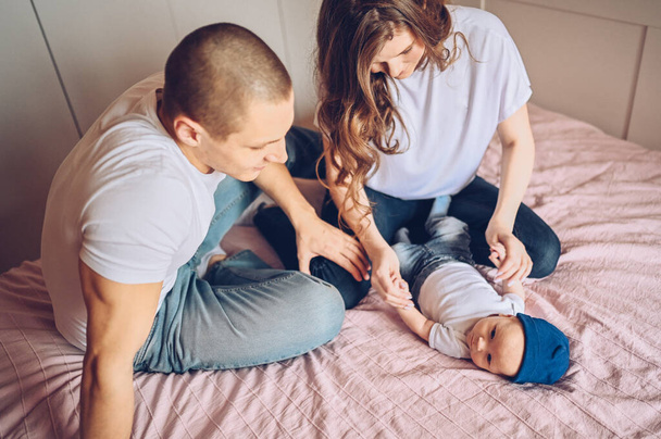 Retrato de cerca de unos padres felices sosteniendo a su bebé. Joven familia feliz, mamá y papá jugando con el pequeño hijo recién nacido emocional lindo en el dormitorio
 - Foto, imagen