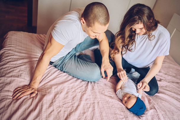 Close up portrait of a happy parents holding their baby. Young happy family, mom and dad playing with cute emotional little newborn child son in the bedroom - Фото, изображение