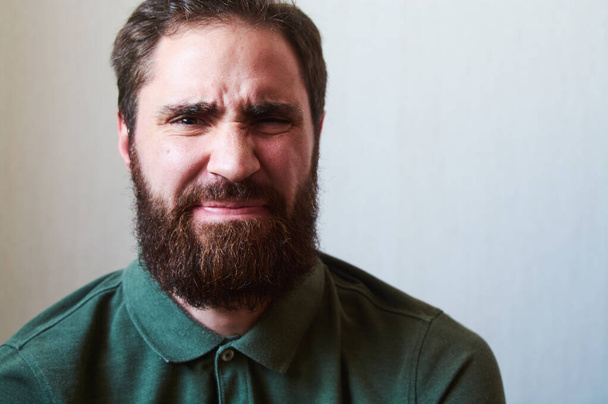 Портрет молодого парня с темной бородой с различными эмоциями на лице в зеленой рубашке
. - Фото, изображение