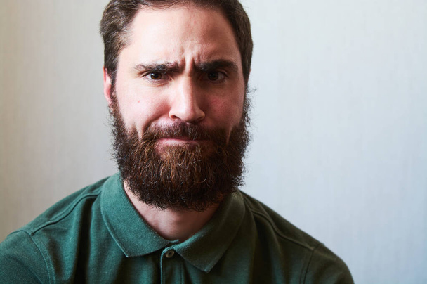 Portré fiatal srác sötét szakállal, különböző érzelmekkel az arcán zöld ingben.. - Fotó, kép