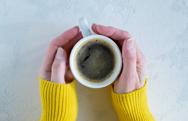 Жіночі руки в яскраво-жовтому теплому светрі тримають білу порцелянову чашку з гарячою кавою. Концепція осіннього, зимового сезону. Горизонтальна орієнтація
. - Фото, зображення