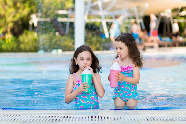 little girls in bright swimsuits drink cocktails near the pool on a Sunny summer day. - Fotoğraf, Görsel