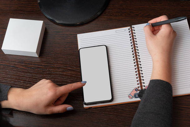 női kéz, egy lány ír egy notebook, használ egy fekete okostelefon, asztali, sötét háttér másolási hely - Fotó, kép