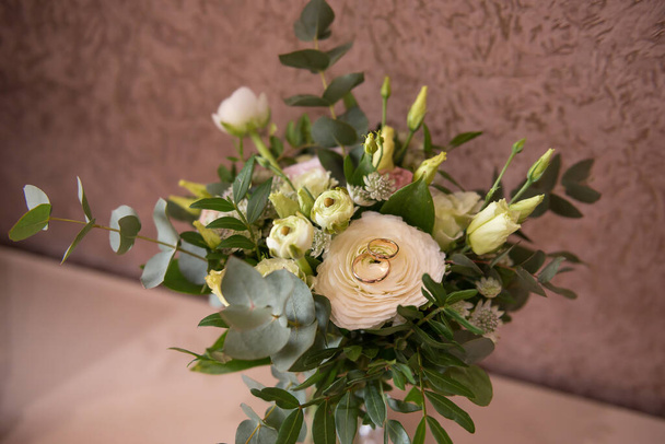 Το μπουκέτο της νύφης. Γάμος. Το πρωινό της νύφης. Κομψό μεγάλο γαμήλιο μπουκέτο με λευκά και πράσινα τριαντάφυλλα και μπουμπούκια και πολλά κλαδιά με πράσινα φύλλα. Σε ένα μεγάλο τριαντάφυλλο υπάρχουν όμορφες βέρες - Φωτογραφία, εικόνα