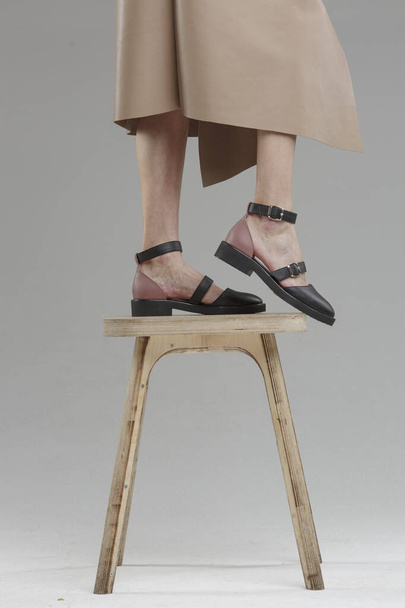 Πόδια σε παπούτσια της όμορφης νεαρής γυναίκας στέκεται στην καρέκλα ενάντια σε απλό τοίχο, δεν μάρκα, αντίγραφο χώρο - Φωτογραφία, εικόνα