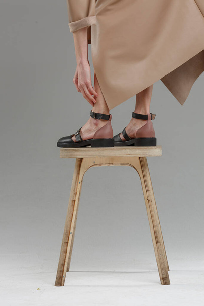 Pernas em sapatos de bela jovem mulher em pé na cadeira contra a parede lisa, sem marca, espaço de cópia
 - Foto, Imagem