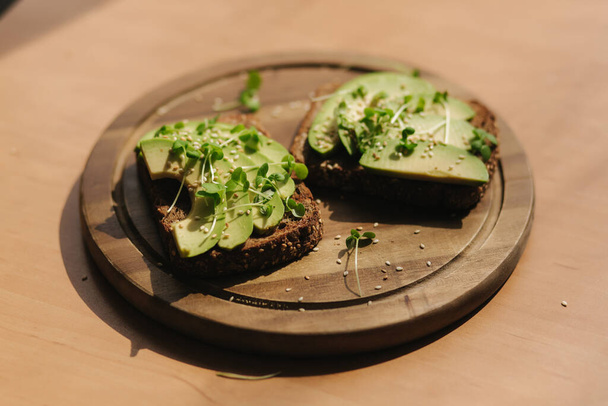 Avocado toast on wooden boadr. Vegetarian food concept. Fresh food at home. Sandwich with avocado and rye toasted bread, sesame seeds and mustard seedings - Фото, изображение