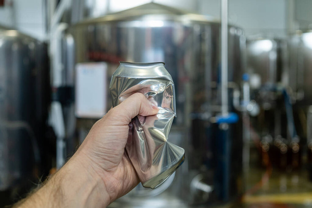 main masculine froisse une boîte en aluminium vide sur le fond de l'équipement de bière. Dans une brasserie
. - Photo, image