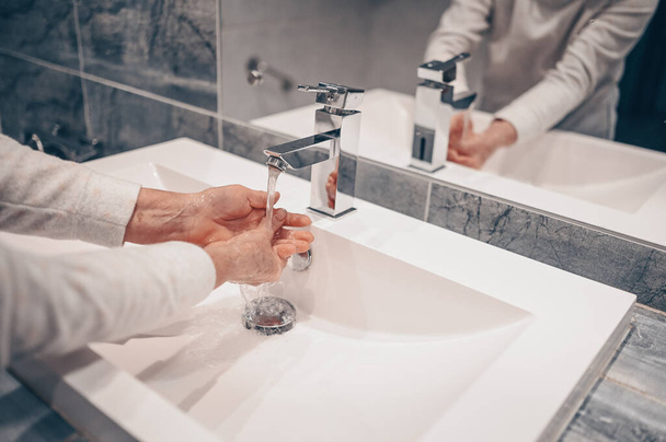 Hand washing lather liquid soap rubbing wrists handwash step senior woman rinsing in water at bathroom faucet sink. Wash hands for COVID-19 spreading prevention. Coronavirus pandemic outbreak. - Photo, Image