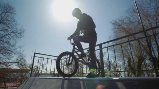 Молодой велосипедист делает трюки в экстремальном парке на закате
 - Кадры, видео