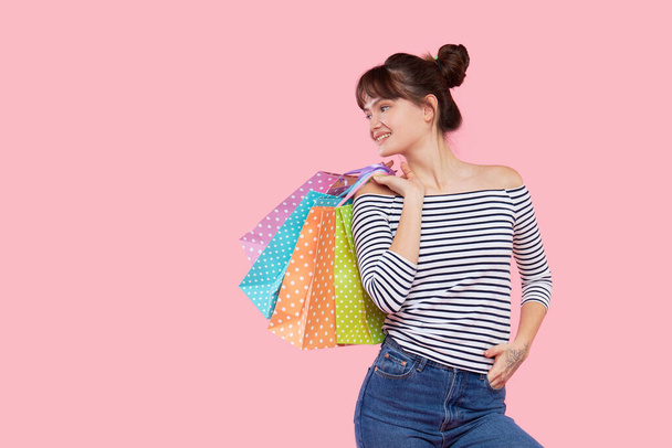 Portrait of a young happy asian woman with shopping bags shows on empty place for text. Pink background - Fotografie, Obrázek