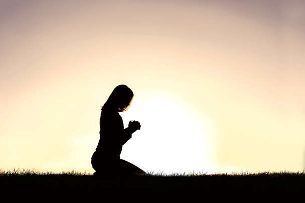 夏の日に祈りの中でひざまずいて若いクリスチャンの女性のシルエット. - 写真・画像