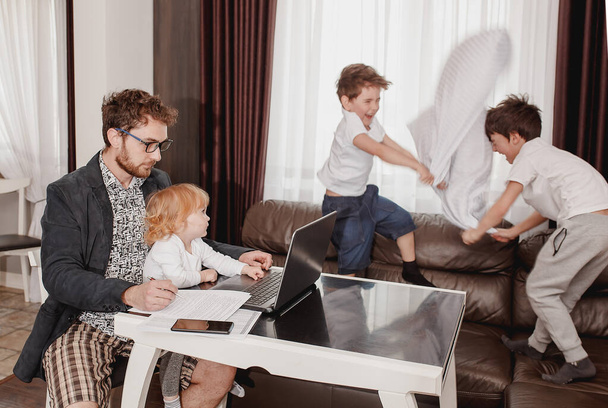 Father businessman try to work at the laptop from home while his children play around. Boys playing pillow fighting. Stressed father. Quarantine time. Stay at home concept. Freelancer - Фото, зображення