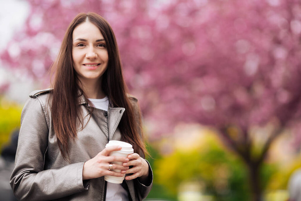 Close-up portrait of a brunette girl on a background of Japanese cherry blossom tree. - Фото, зображення