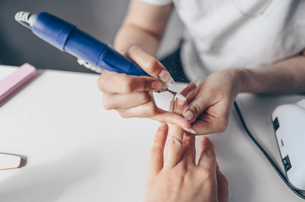 Hardware professional manicure process, cleaning of nails by a milling cutter. Close up female hands in beauty salon. Finger nail treatment, making process. Electric nail file drill in action - Fotografie, Obrázek
