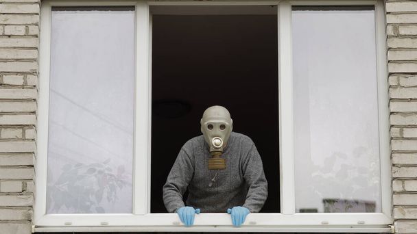 Ein alter Mann mit Gasmaske steht isoliert zu Hause am Fenster und steht unter Quarantäne. Coronavirus - Foto, Bild
