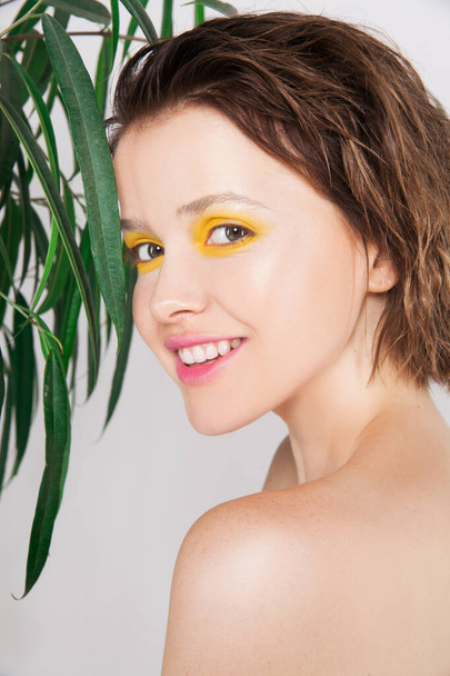 Excited young girl smiling with perfect skin and teeth with fresh yellow color makeup and green plant. Natural beauty woman amazed. Expressive facial expressions. Skincare beauty spa treatment concept - Photo, Image