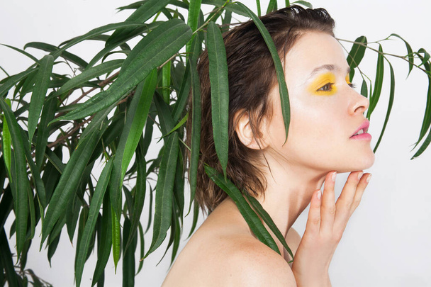 新鮮な黄色の色のメイクと緑の植物と完璧な肌を持つ美しい若い十代の女の子。自然美の女。スキンケアフェイスケア美容室スパトリートメントコンセプト - 写真・画像