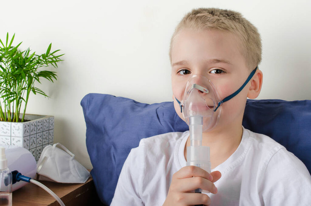 Хворий хлопчик дихає через інгаляторну маску. Використання туманності та інгалятора для лікування або профілактики респіраторних захворювань, таких як коронавірус, астма та алергія. Терапія в домашніх умовах
. - Фото, зображення