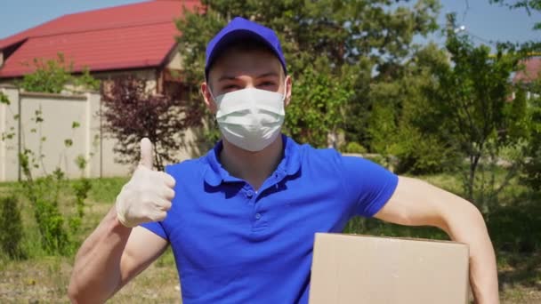 mężczyzna kurier z usługi dostawy w masce medycznej i rękawiczki pokazuje kciuk w górę - Materiał filmowy, wideo