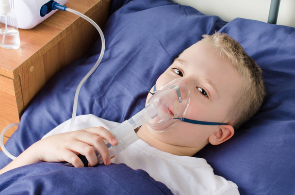 Kranker Junge atmet durch Atemmaske. Verwendung von Vernebler und Inhalator zur Behandlung oder Prävention von Atemwegserkrankungen wie Coronavirus, Asthma und Allergien. Therapie zu Hause. - Foto, Bild