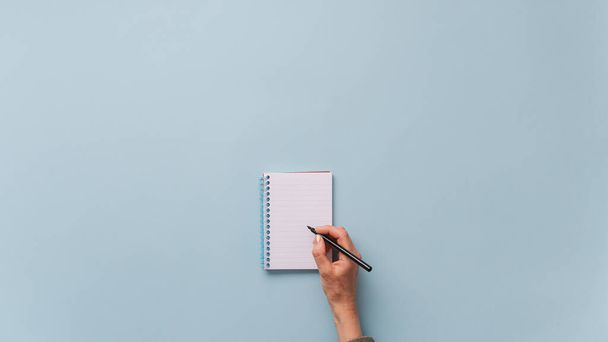 Vista superior de la escritura a mano femenina en bloc de notas en blanco con marcador negro. Sobre fondo azul claro con mucho espacio de copia
. - Foto, imagen