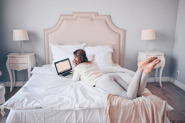 Young european woman working on a laptop in white bedroom during coronavirus isolation home quarantine. Pandemic Corona virus. Distance online work from home. COVID-19 concept promote stay safe home - Foto, Imagem