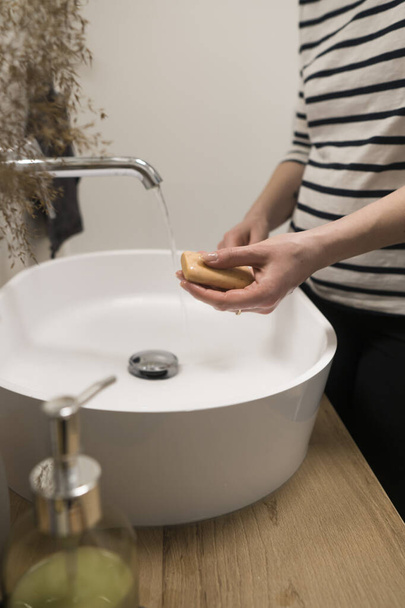 COVID-19コロナウイルス。泡石鹸で手を洗う女性とバスルームでお湯。衛生的で、コロナウイルスを予防する。手を掃除することによるコロナウイルスのパンデミック保護. - 写真・画像