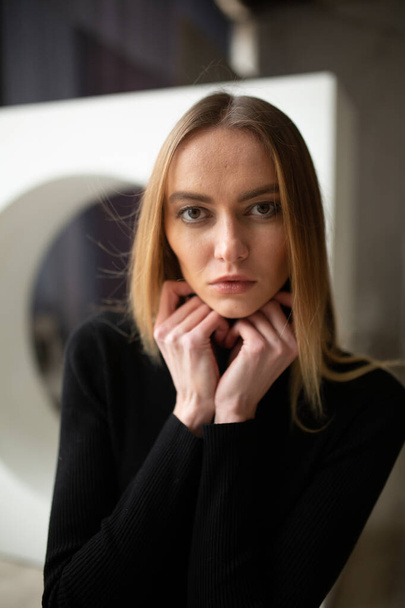 close up portrait of stylish looking girl in black turtleneck with blue eyes, model posing in interior, studio background  - Photo, Image