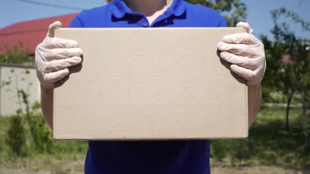 A male courier delivery man in medical gloves is holding a cardboard box - Footage, Video