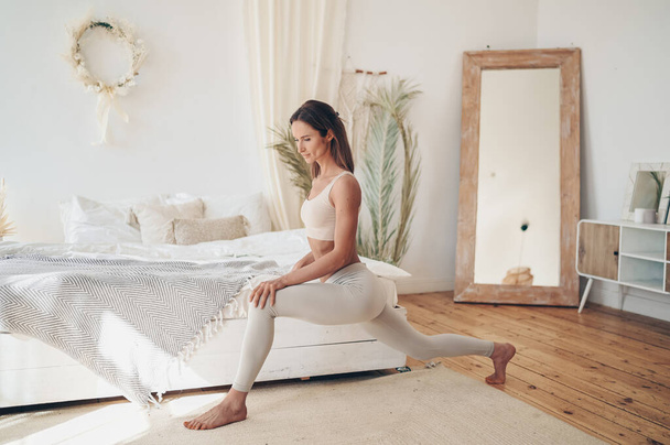 Evde fitness. Genç sporcu sıska kadın sabah yoga egzersizleri yapıyor yatak odasında kendini izole karantinada. COVID-19 konsepti evde güvende kalmanızı sağlar. Hayat kurtarır. Sağlıklı vücut yaşam tarzı - Fotoğraf, Görsel
