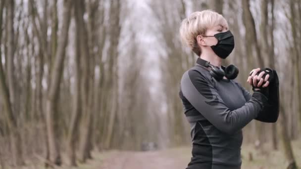 A middle-aged woman in a mask is doing morning exercise outside - Záběry, video