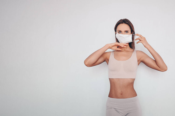 Evde fitness. Spor kıyafetleri giyen zayıf bir kadın kendini karantinaya alırken maske takıyor. COVID-19 konsepti evde güvende kalmanızı sağlar. Hayat kurtarır. Metin düzenleme pankartı için boş alan - Fotoğraf, Görsel