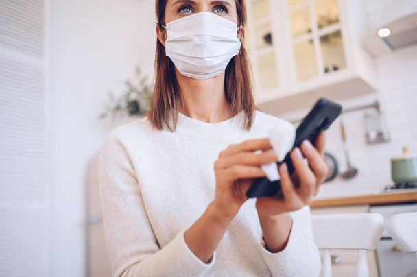 顔保護マスク洗浄携帯電話の欧州の女性は、手の消毒剤で細菌Covid-19を排除するために、コロナウイルスに汚染を避けるためにアルコールと綿ウールを使用して. - 写真・画像
