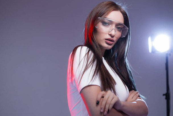 Portrait of a stylish european woman in a white T-shirt with transparent glasses and arms crossed on her chest. Red Light in the background. - Fotografie, Obrázek
