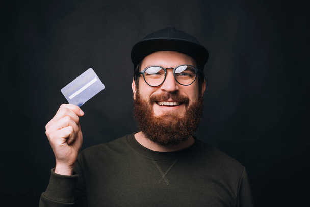 カードを使え。ひげを生やした男は青いクレジットカードやデビットカードを持ちながら笑っている. - 写真・画像