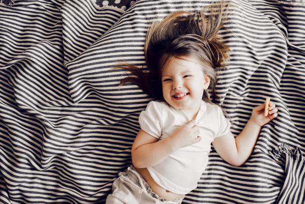Portrait of beautiful cute little 3 years girl lying on bed in dress and looking at the camera - Фото, изображение