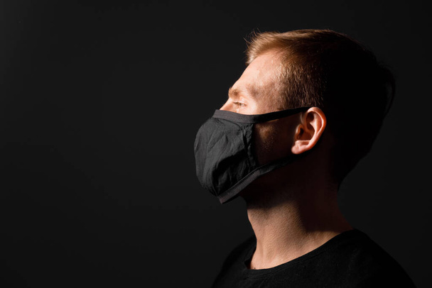 Handsome man in black t-shirt wear black medical mask, gray background. Coronavirus covid-19 quarantine period concept - Photo, Image