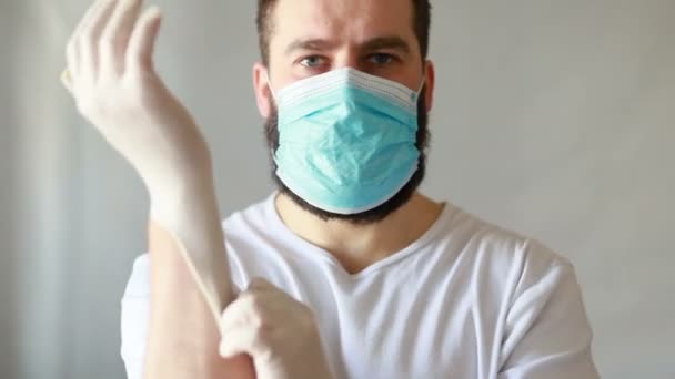 A man in a protective mask coughs. The man is sick, colds, cough. Caucasian bearded man in white protective suit looks at the camera and puts a medical mask on face. Close up - 映像、動画