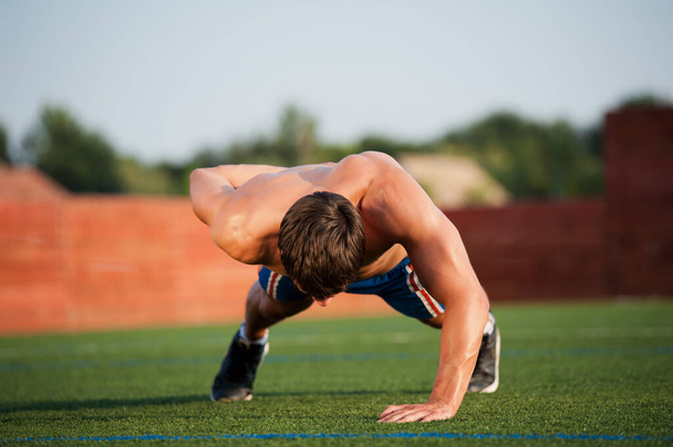 Szabadtéri sport, fitnesz edzés. Jóképű fiatal férfiak fekvőtámaszoznak a sportpályán egy napsütéses napon. - Fotó, kép