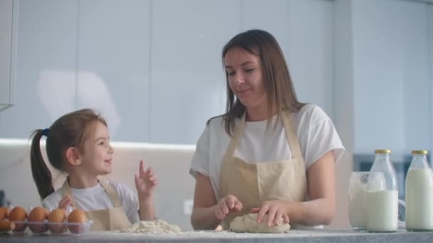Daughter and mother at home in the kitchen in aprons indulge and have fun give five and sprinkle with flour - Footage, Video