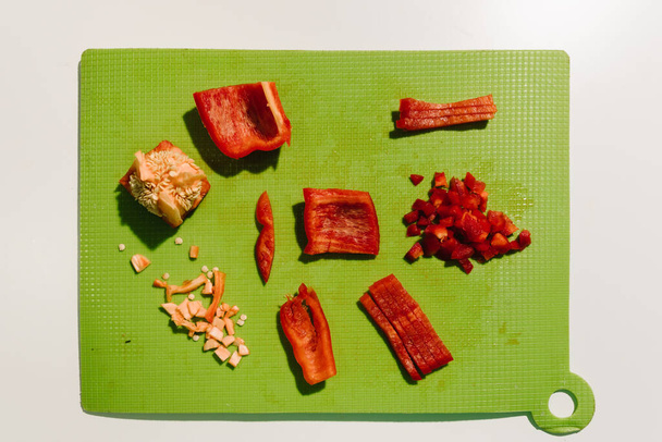 Vue du dessus d'une composition de poivron rouge haché sur une planche à découper verte, sur une table blanche. Espace de copie
. - Photo, image